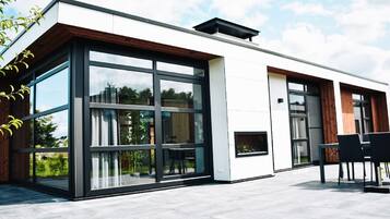 Ein modernes Gebäude mit großen Glasfenstern, einer flachen Dachkonstruktion und einer Terrassenfläche mit Gartenmöbeln.