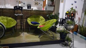 Una cocina con armarios de madera, una silla negra y una silla verde con cojín. Hay plantas en macetas y una pequeña mesa con una silla.