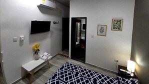 Un dormitorio con una cama, una mesita de noche con un florero, un ventilador de techo, un televisor montado y un espejo.