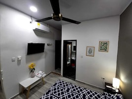 Un dormitorio con una cama, una mesita de noche con un florero, un ventilador de techo, un televisor montado y un espejo.