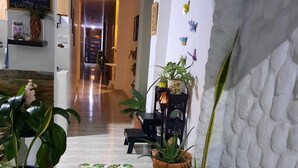 Vestíbulo de hotel con suelo de baldosas, plantas en macetas, un banco y una pared decorada con mariposas.