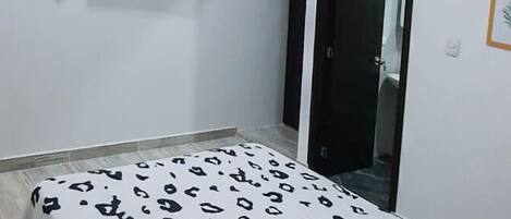 Ein Schlafzimmer mit Bett, Deckenventilator, Klimaanlage, einem an der Wand befestigten Fernseher und einer Tür.