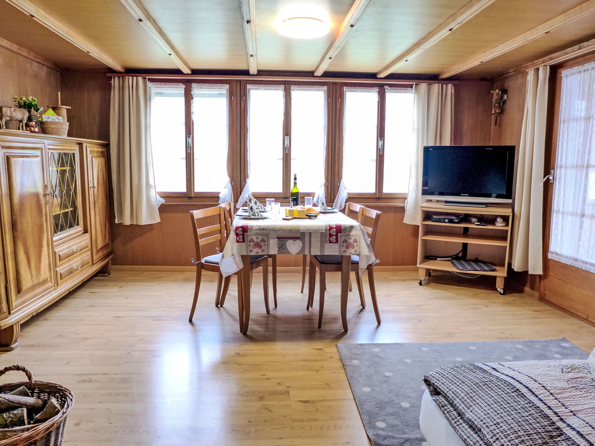 Ein Essbereich mit Holztisch, Stühlen und einem Fernseher auf einem Holzgestell.