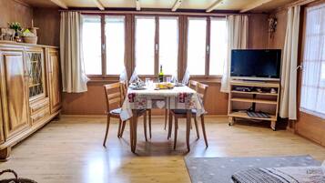 Ein Essbereich mit Holztisch, Stühlen und einem Fernseher auf einem Holzgestell.