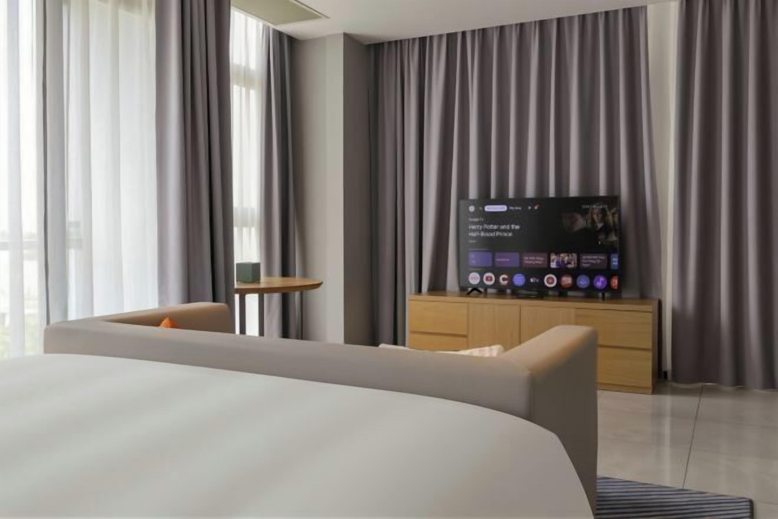 A modern hotel room with a large bed, a television, a small table, and a wardrobe.