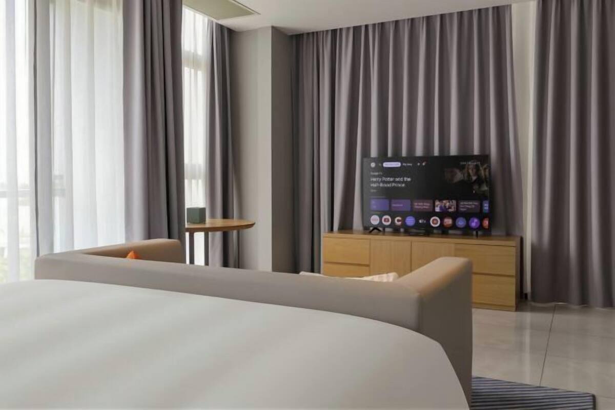 Une chambre d’hôtel moderne avec un grand lit, un téléviseur posé sur une commode en bois, une petite table et un canapé.