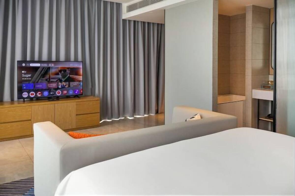 Une chambre d’hôtel moderne équipée d’un grand téléviseur à écran plat, d’un canapé, d’un lit et d’un espace douche.