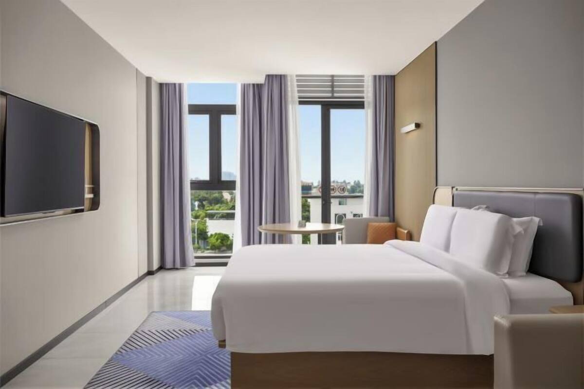 Une chambre d’hôtel avec un lit, une télévision, un balcon avec des rideaux et une vue sur la ville.