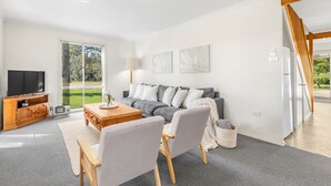 A modern living room with a grey sofa, wooden coffee table, and a TV on a wooden stand. - Madigan Cottages | Settlers Cottage (Lovedale)