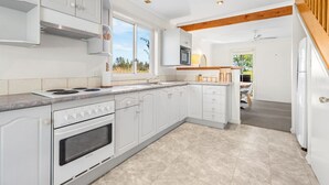 A modern kitchen with white cabinetry, a stove, and a microwave. - Madigan Cottages | Settlers Cottage (Lovedale)