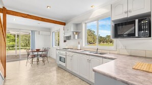 A modern kitchen with white cabinetry, a built-in microwave, and a dining area with a table and chairs. - Madigan Cottages | Settlers Cottage (Lovedale)