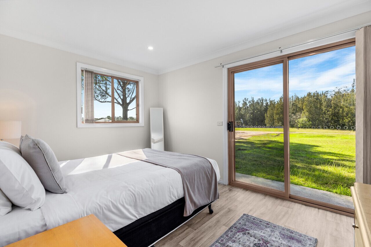 Ein Schlafzimmer mit Bett, Fenster mit Blick auf einen Baum und einer Glastür zu einer Rasenfläche.