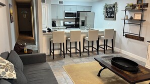 A modern kitchen with white cabinets, a central island with bar stools, and a dining area with a dark wooden table and a patterned rug. - Waterfront modern condo on Walden at the lake Conroe (Montgomery)