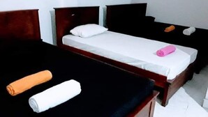 A room with two single beds, each with a wooden headboard and white bedding. There are two rolled towels, one orange and one white, placed on the beds. - Black And White Kandy Guest House  (Kandy)