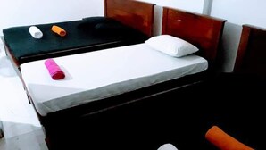 A single bed with a white mattress, a wooden headboard, and a black headboard. There are two pillows, one white and one orange. - Black And White Kandy Guest House  (Kandy)