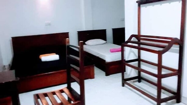 A small, compact room with two single beds, a wooden chair, and a wooden rack. - Black And White Kandy Guest House  (Kandy)