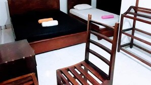 A small, simple room with two wooden beds, a wooden chair, and a small table. - Black And White Kandy Guest House  (Kandy)