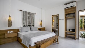 A modern bedroom with a wooden bed, bedside tables, a bench, pendant lights, a ceiling fan, and built-in shelving. - Villa Oasi 2 by Alfred in Bali (Pecatu)