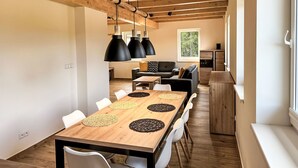 Ein moderner Essbereich mit einem Holztisch und Stühlen, schwarzen Pendelleuchten und Blick zur Küche im Hintergrund.