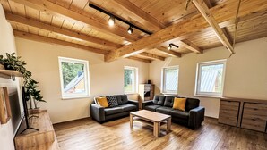 Ein geräumiges Wohnzimmer mit Holzdielen, einer Sofagarnitur, einem Couchtisch und großen Fenstern.
