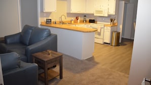 Um espaço compacto com cozinha compacta, sofá, mesa de centro pequena e lixeira.