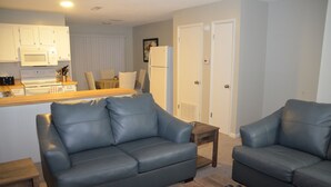 Espaço compacto para viver, com cozinha americana, dois sofás, uma mesa de centro e uma porta que dá para outro quarto.