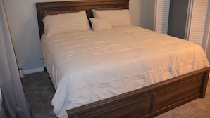 Uma cama bem arrumada com cabeceira de madeira, piso coberto por carpete e um armário fechado ao fundo.