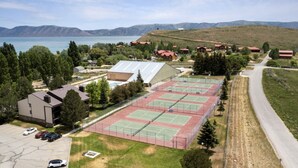 A tennis court complex with multiple courts, a parking area, and buildings with red roofs.