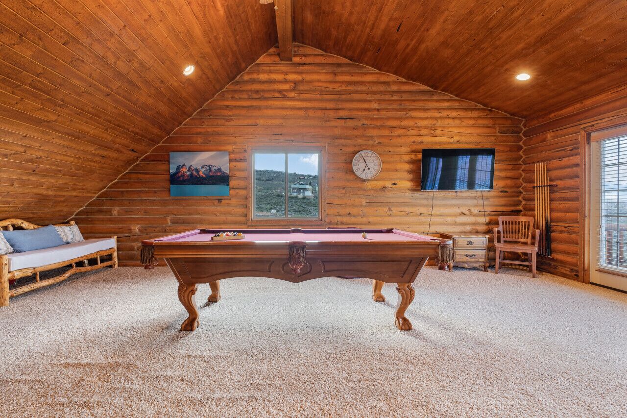 A wooden cabin with a pool table, a sofa, and a window with a view.