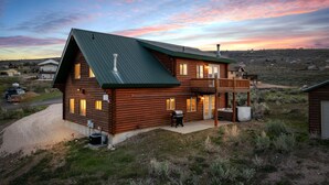 A log cabin with a green roof, a deck, and a garage.