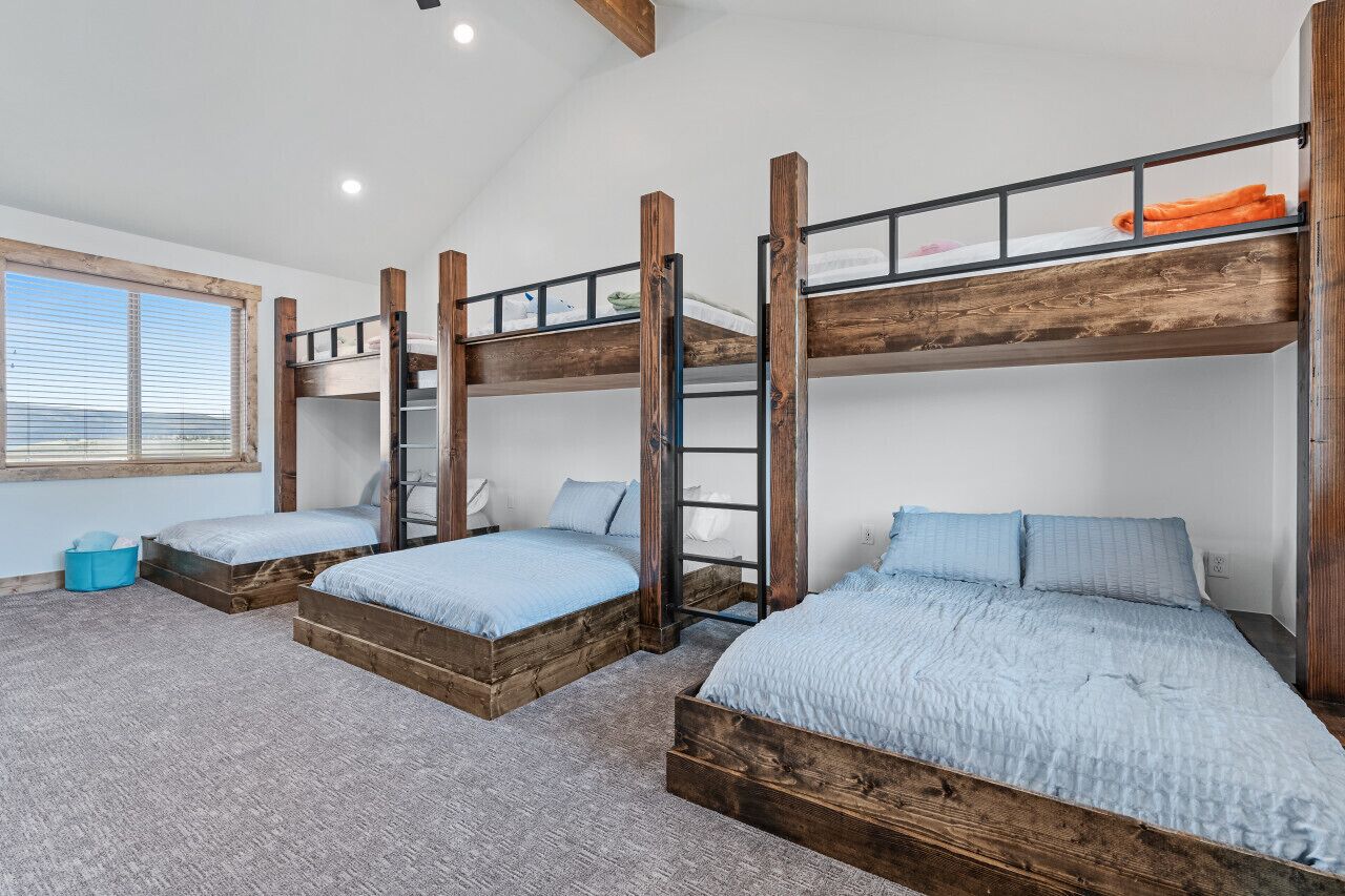 A room with three bunk beds, a window with blinds, and a blue storage bin.