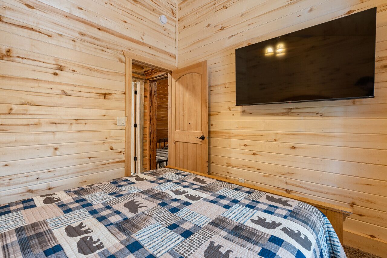 Une pièce aux murs lambrissés, avec un lit, une porte donnant sur une autre pièce et un téléviseur fixé au mur.