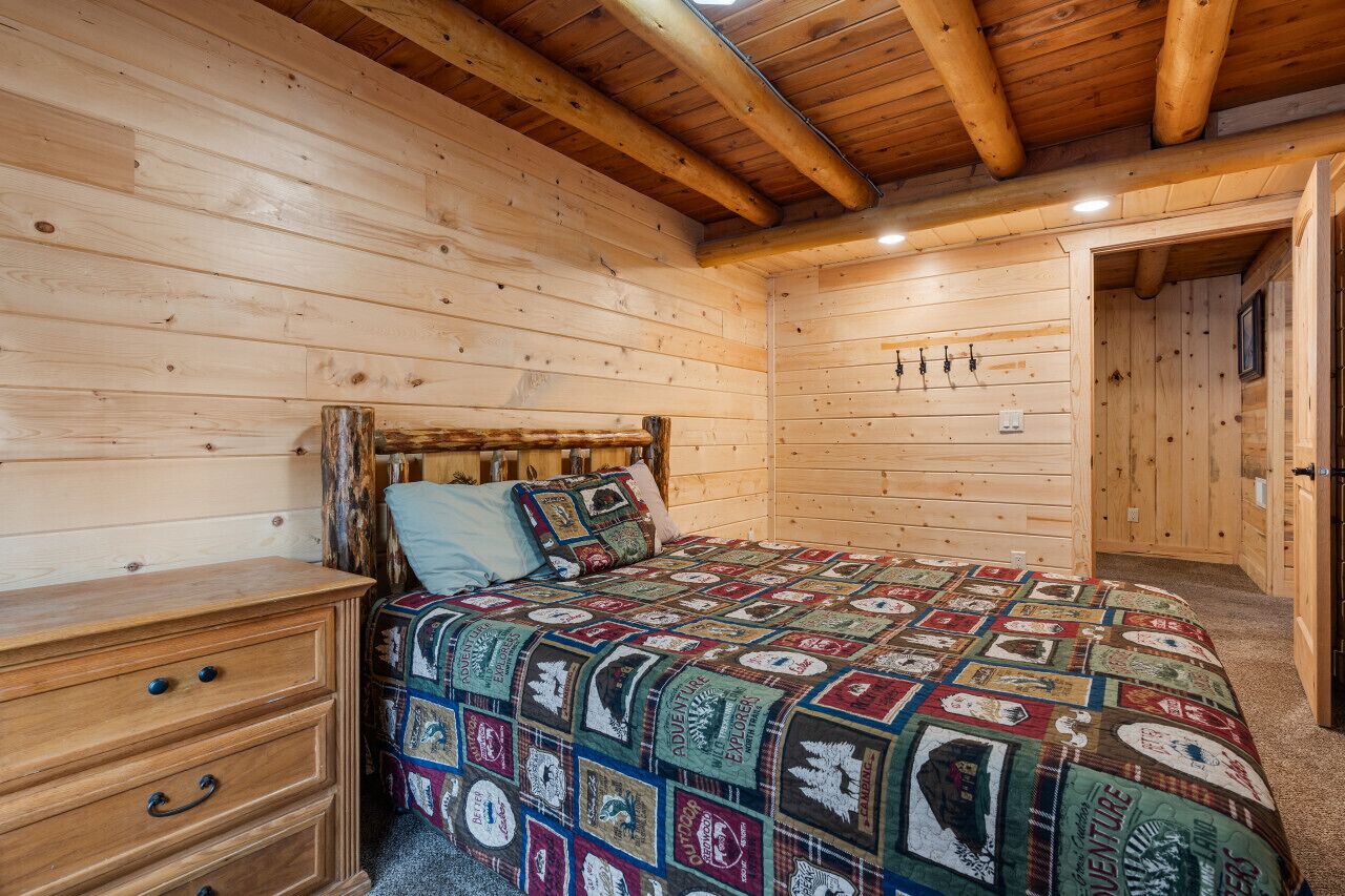 Un dormitorio rústico de cabaña de troncos con una cama de madera, un aparador y un colcha con parches con motivos de aventura.