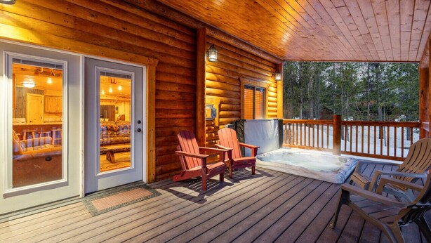 A wooden deck with Adirondack chairs, a hot tub, and a view of the surrounding forest.