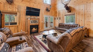 A log cabin interior with a fireplace, leather sofas, and mounted animal heads.