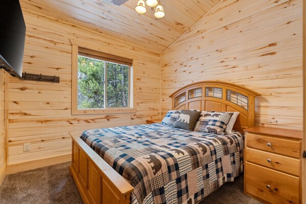 Un dormitorio de cabaña de madera con una cama, una mesita de noche, una ventana y un ventilador de techo.