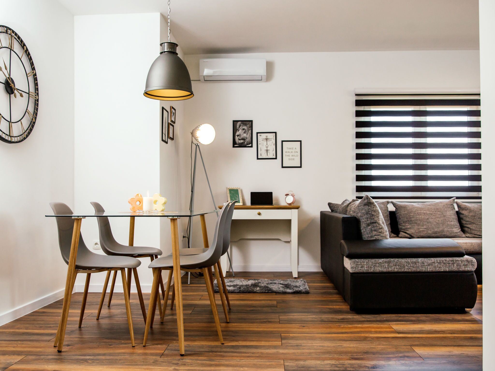 Un salon moderne avec une table à manger en verre, deux chaises, un canapé noir, un lampadaire et une horloge murale.