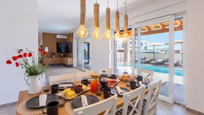 Ein moderner Essbereich mit Blick auf den Pool, Holzpendelleuchten und einem Frühstücksbuffet.