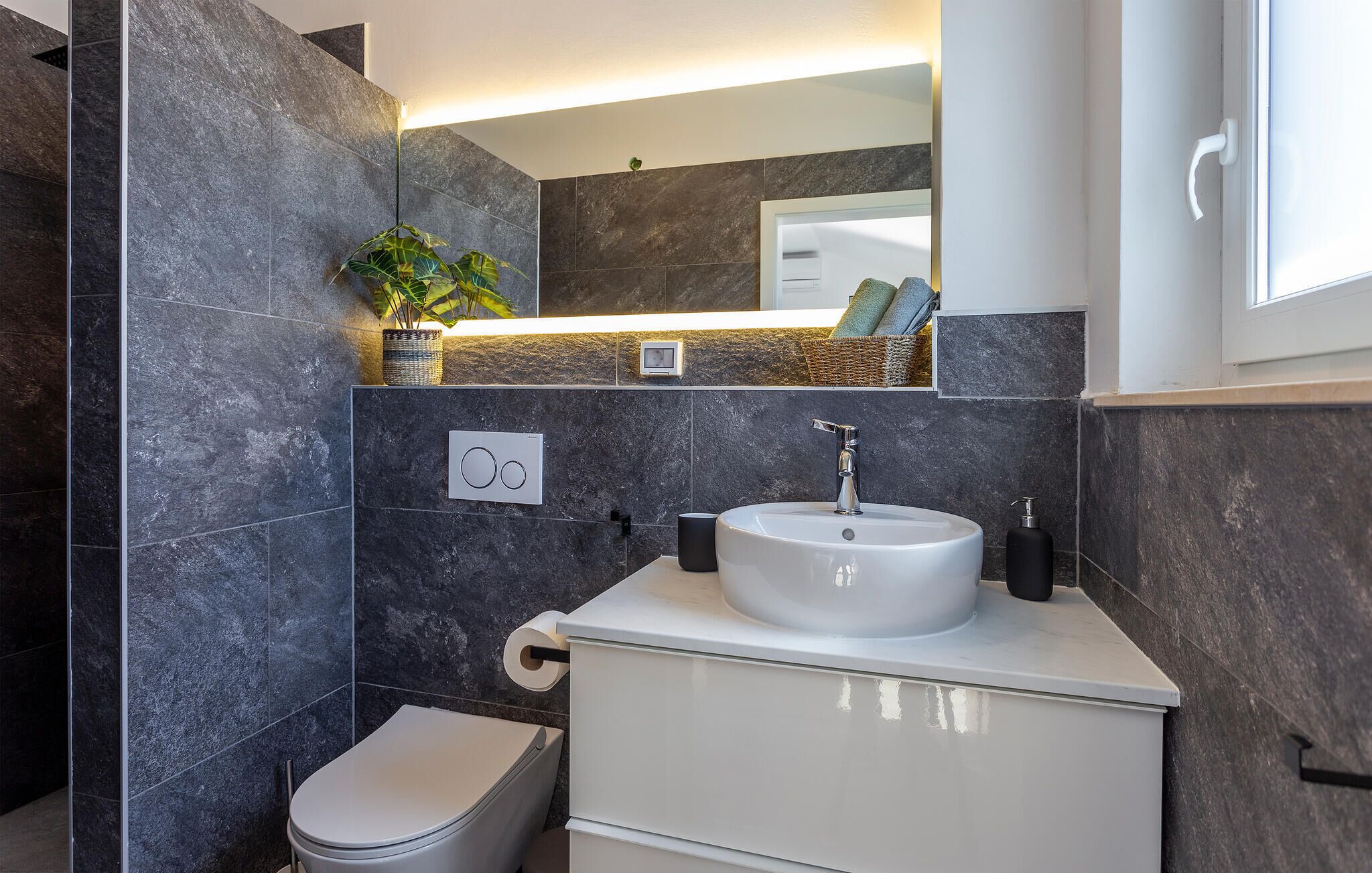 A modern bathroom with dark marble tiles, a white sink, and a toilet.