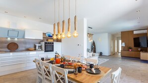 Eine moderne Küche mit weißen Schränken, einem eingebauten Backofen und einem Essbereich mit einem Holztisch und weißen Stühlen.