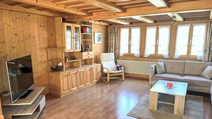 Ein gemütliches Wohnzimmer mit Holzwänden und -decke, einem Flachbildfernseher, einer Couch, einem Sessel und einem Couchtisch.