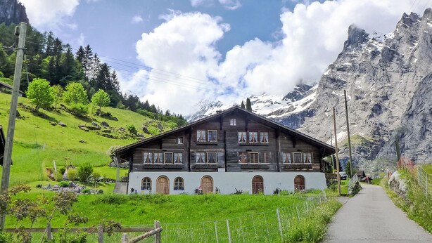 Ein traditionelles Chalet mit geneigtem Dach, vielen Fenstern und einem Weg davor.
