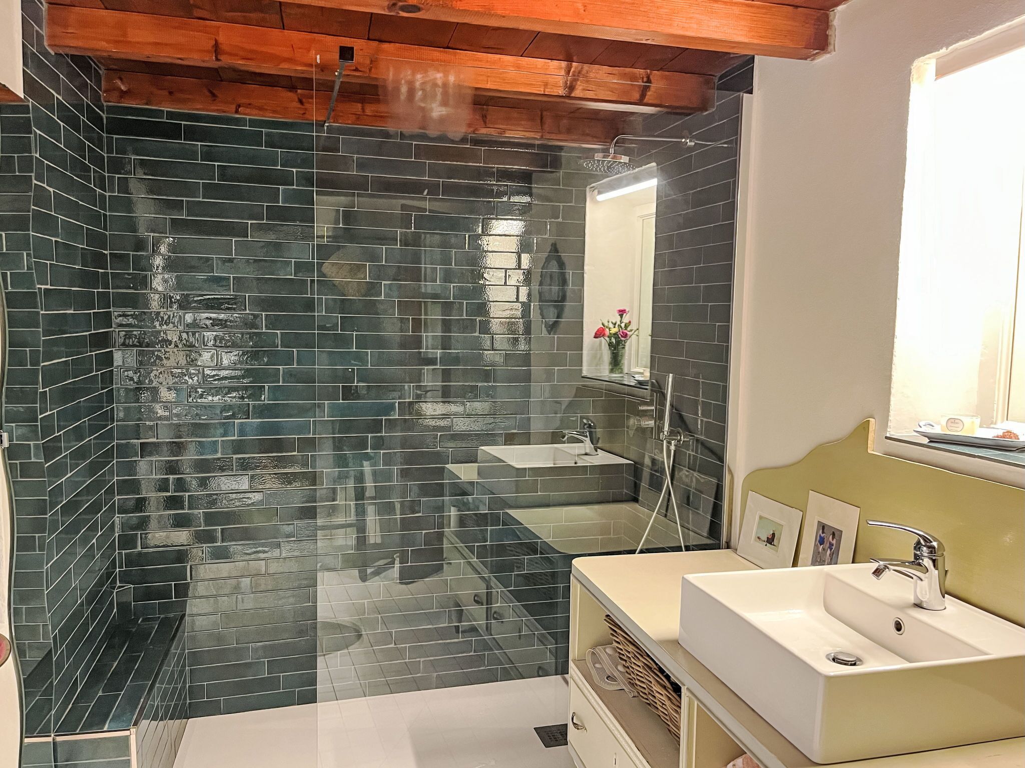 A modern bathroom with dark tiled walls, a glass shower enclosure, a sink, and a mirror.
