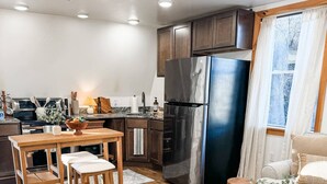 Une cuisine moderne équipée d’appareils électroménagers en acier inoxydable, un coin repas avec des meubles en bois et un espace de vie chaleureux comprenant un canapé et des poufs.