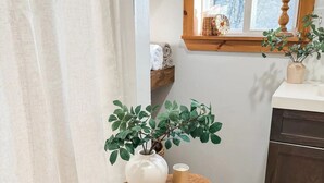 Un coin de pièce avec un tabouret en bois, un vase blanc et une plante en pot.