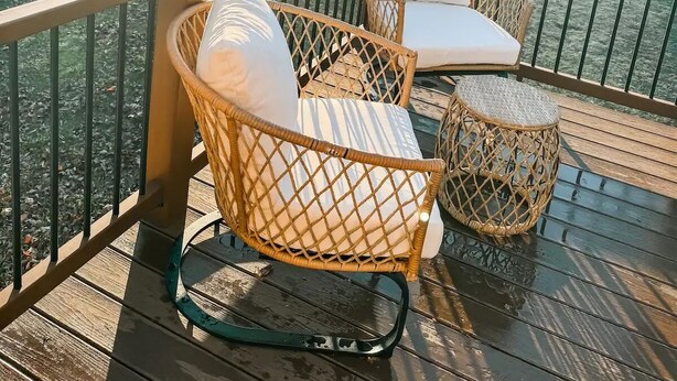 Une terrasse en bois, dotée de chaises et de coussins en osier, qui offre une vue sur une étendue d’eau et des arbres.