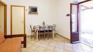 A dining area with a table set for four, a television mounted on the wall, and a door leading to an outdoor area. - Casa Bartolomea - CASA BARTOLOMEA 11 (Marina di Campo)