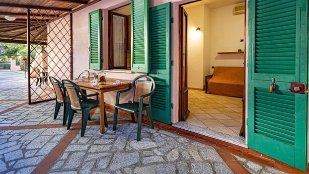 A covered outdoor seating area with a table and chairs, a wooden ceiling, and green shutters on the walls. - Casa Bartolomea - CASA BARTOLOMEA 11 (Marina di Campo)