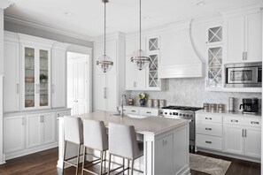 Una cocina moderna con armarios blancos, una isla central con taburetes de bar, una estufa de acero inoxidable y un microondas.