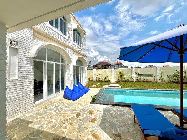 Relax by the pool surrounded by a patio with a geometric pattern and enjoy the shade from the umbrella.